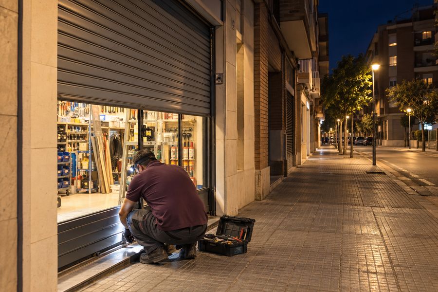 Técnico desbloqueando de noche la cerradura de un cierre metálico que no baja